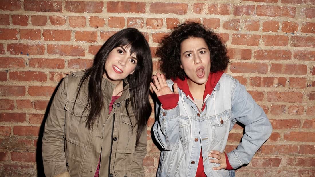 Comedians Abbi Jacobson and Ilana Glazer posing against a brick wall