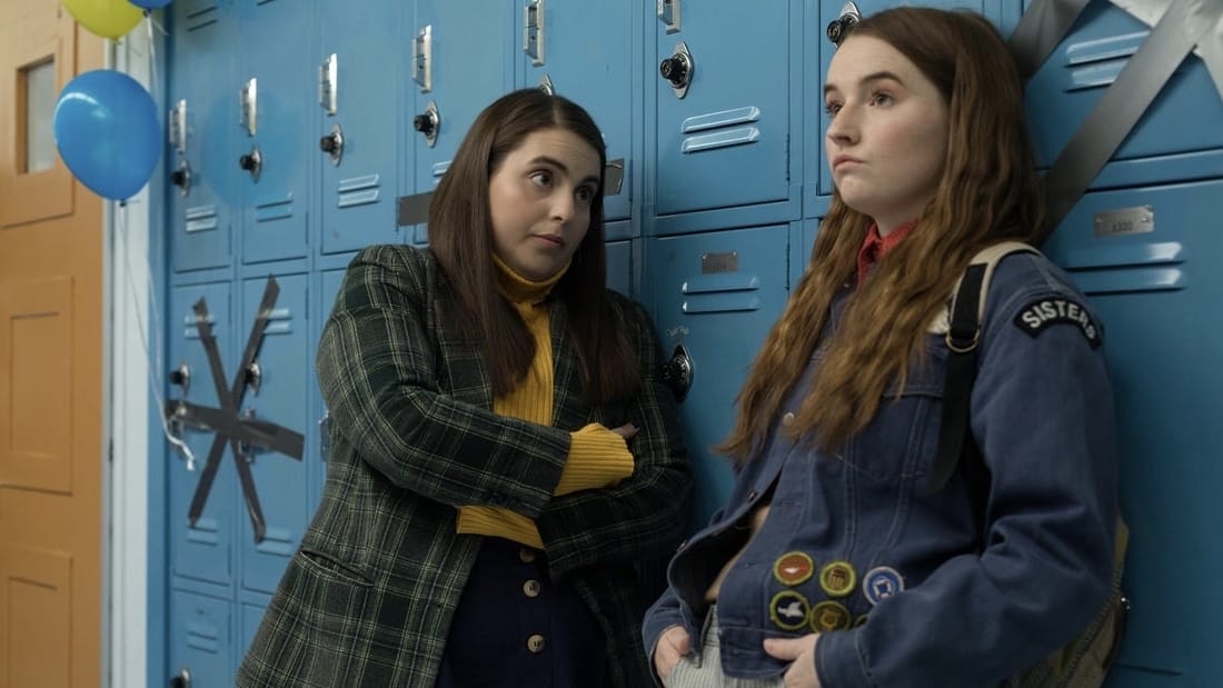 Beanie Feldstein and Kaitlyn Dever standing against blue lockers in the movie Booksmart.