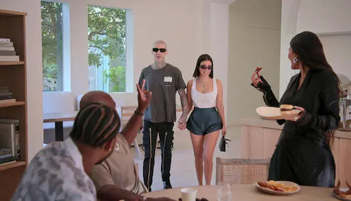 Still image from The Kardashians S1 Episode 101 ‘Burn Them All to the F*cking Ground’ featuring Kourtney and Travis walking into the kitchen where two men and Kim turn to wave